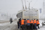 Работники коммунальных служб толкают троллейбус во время сильного снегопада