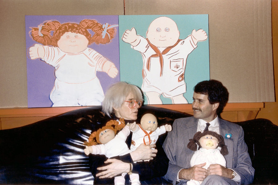 Энди Уорхол держит кукол бренда Cabbage Patch Kids на&nbsp;фоне своих картин, изображающих этих кукол, 1985&nbsp;год