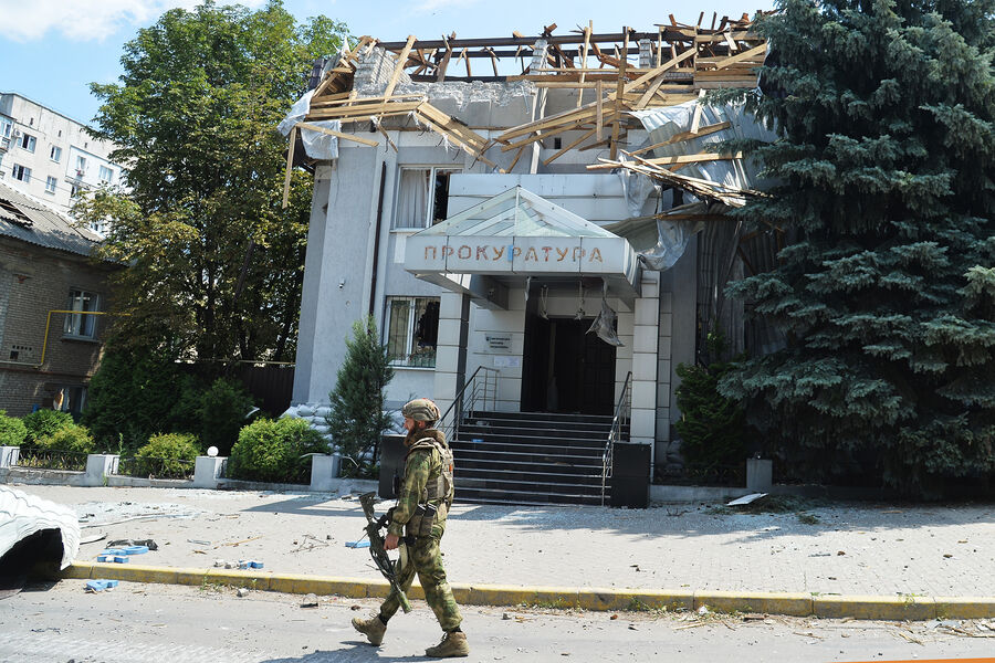 Боец специального полка полиции имени Героя России Ахмата-Хаджи Кадырова идет рядом с&nbsp;разрушенным зданием Лисичанской окружной прокуратуры, июль 2022&nbsp;года