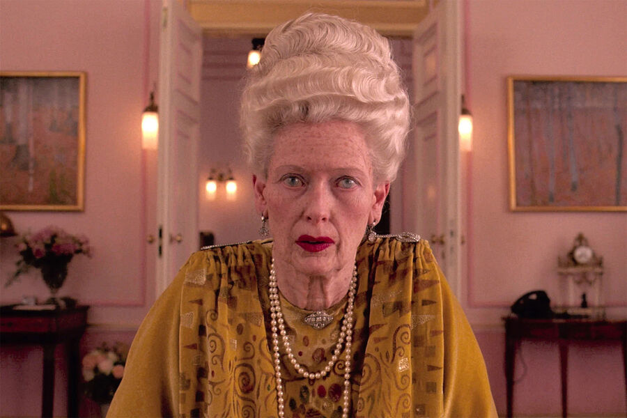 <b>&laquo;Отель &laquo;Гранд Будапешт&raquo; (2014)</b>
<br><br>
Вторая работа Тильды Суинтон с&nbsp;Уэсом Андерсоном (всего их аж пять, включая также &laquo;Остров собак&raquo;, &laquo;Французский вестник&raquo; и &laquo;Город астероидов&raquo;) стала, пожалуй, самой яркой в&nbsp;их творческом тандеме. В&nbsp;центре сюжета &mdash; история консьержа роскошного отеля &laquo;Гранд Будапешт&raquo; мсье Густава (Рэйф Файнс), который вместе со своим юным другом, портье Зеро Мустафой (Тони Револори), оказывается втянут в&nbsp;запутанную историю, полную интриг, краж и убийств, связанных с&nbsp;наследством богатой постоялицы &mdash; графини Селин-Вильнев Дегофф-унд-Таксис (Тильда Суинтон). Для&nbsp;роли пожилой графини 54-летняя актриса полностью преобразилась, однако даже за&nbsp;гримом легко угадывается ее фирменная мимика.