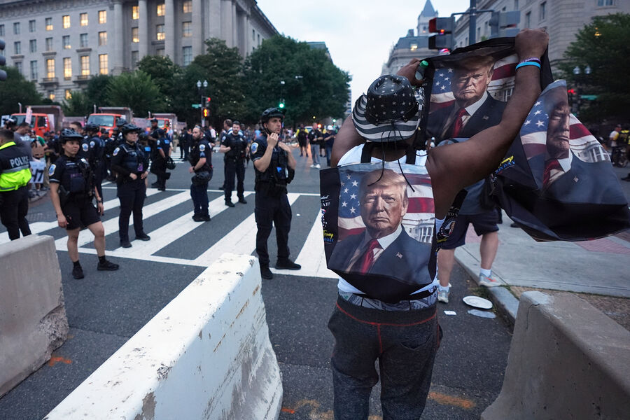 Поддерживающий политику Дональда Трампа размахивает портретом президента перед&nbsp;протестующими в&nbsp;день военного парада, посвященного 250-летию армии США, Вашингтон, 14&nbsp;июня 2025&nbsp;года