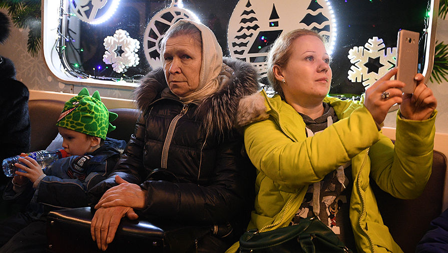 Пассажиры в новогоднем поезде московского метро, украшенном гирляндами и еловыми ветками